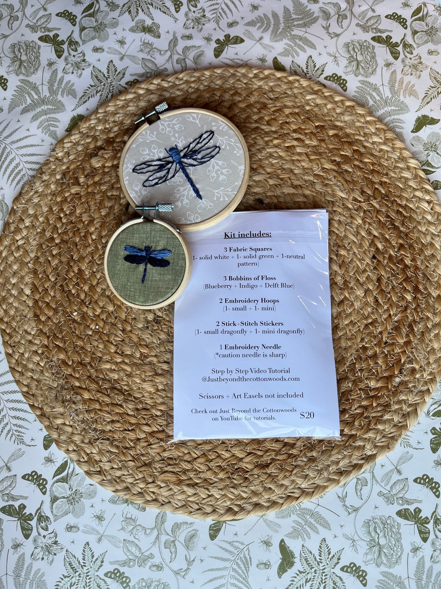 Embroidery kit with dragonfly designs with list of what is included in kit on a woven mat and patterned background