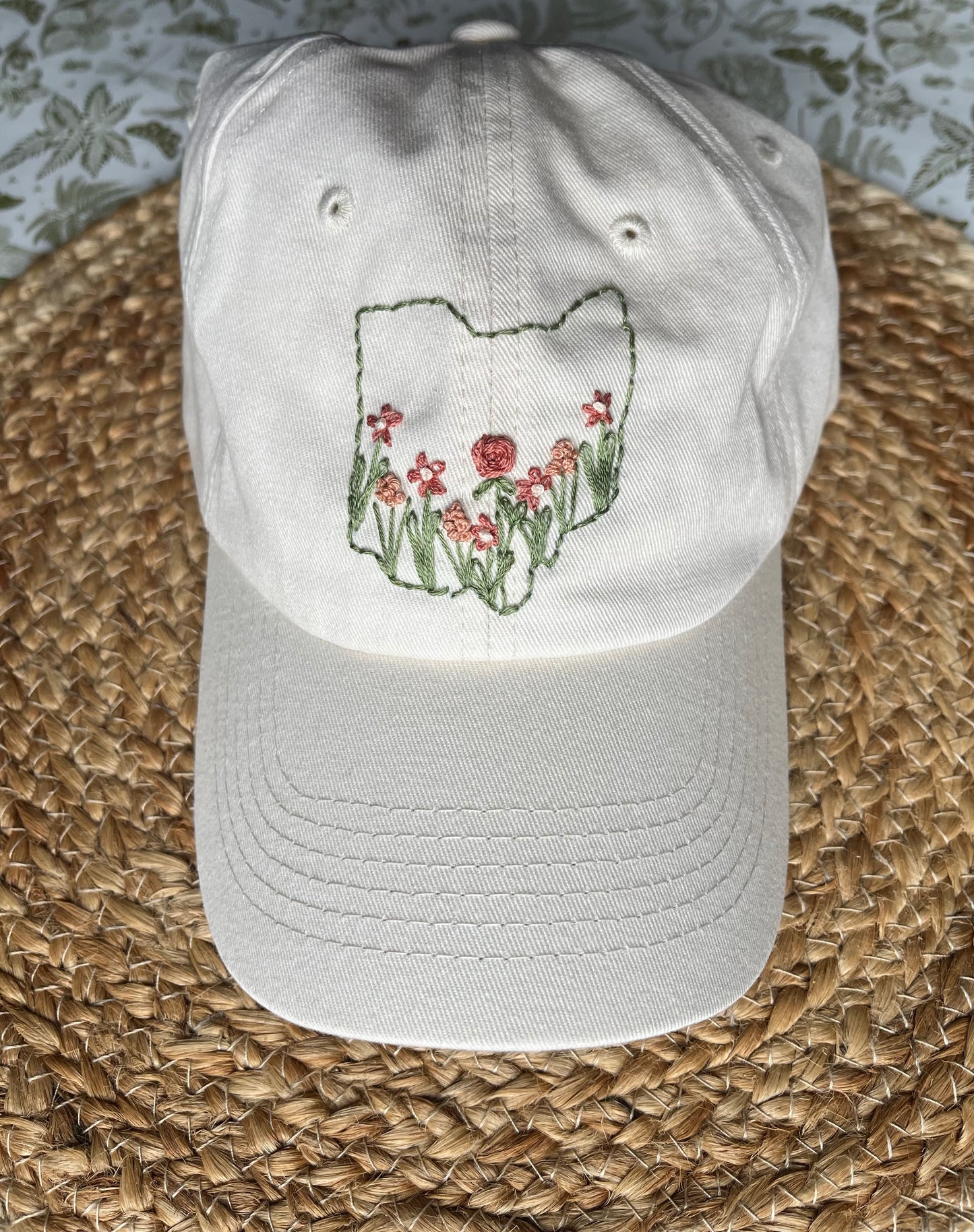 Hand embroidered hat on woven mat with green and white floral background
