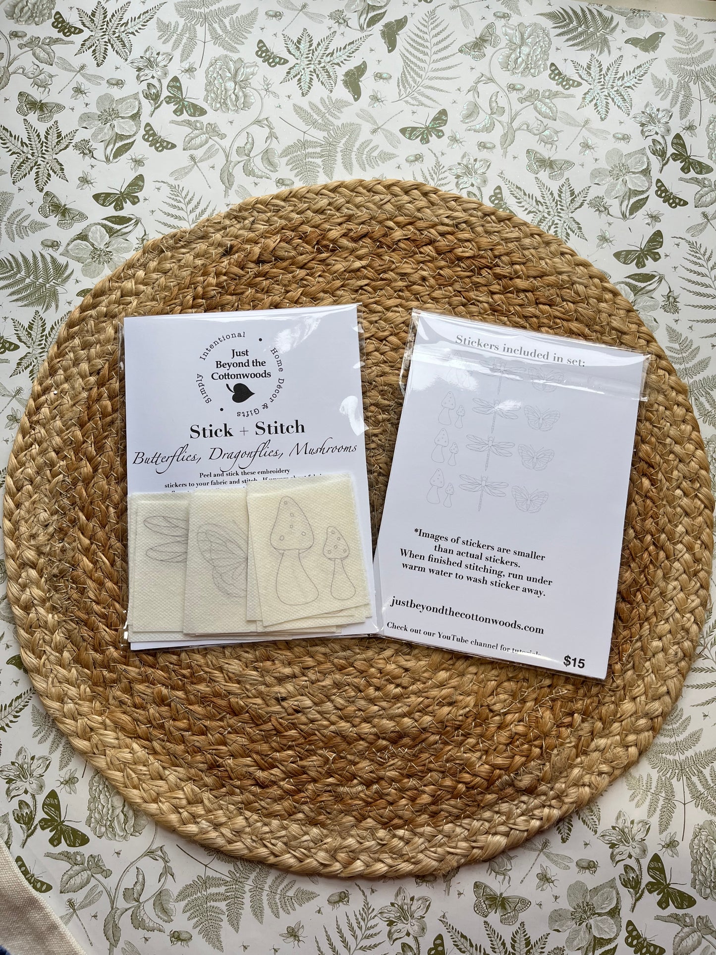 Two packets of 'Stick & Stitch embroidery stickers on a woven mat with a floral-patterned background.