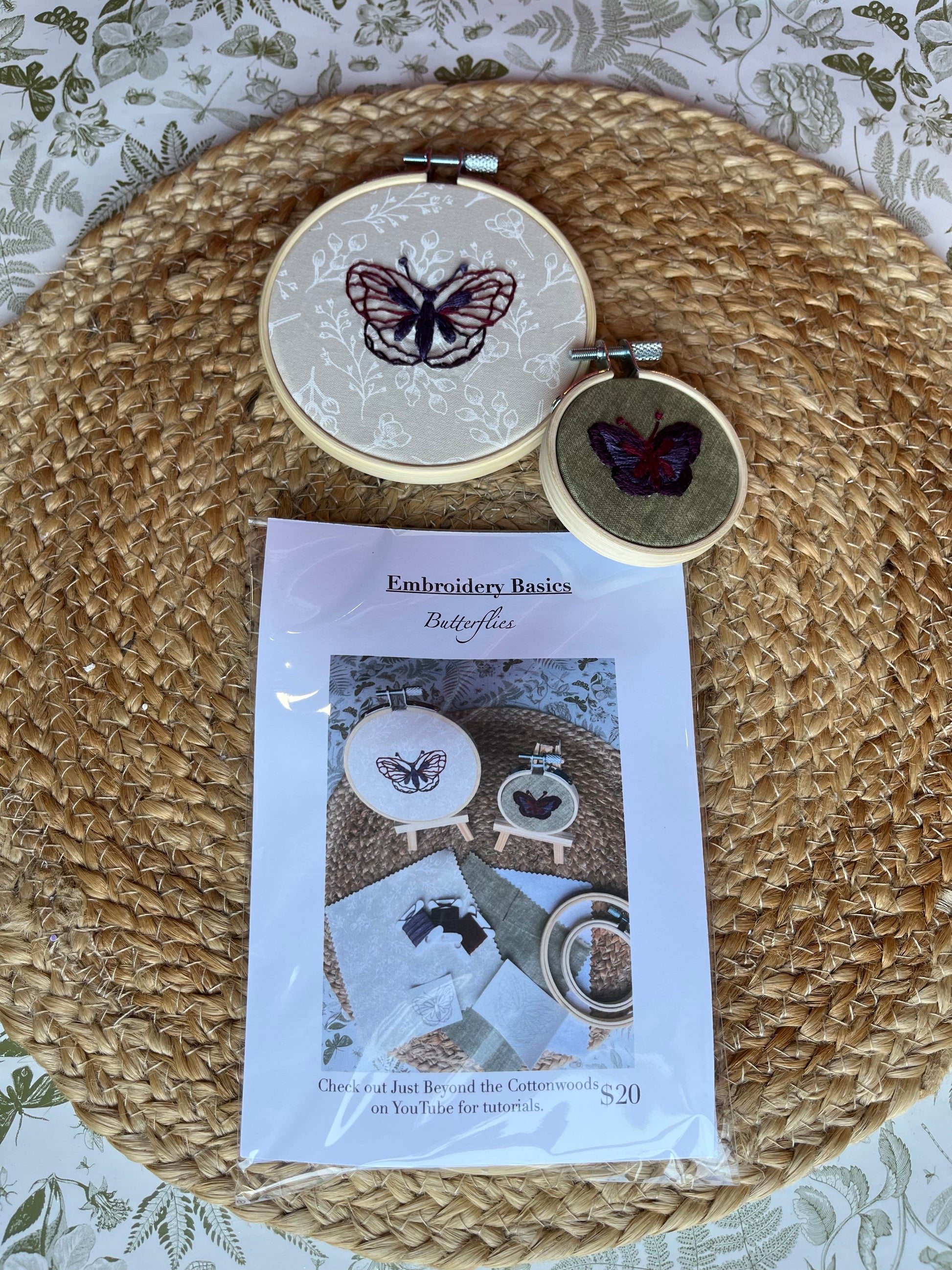 Two embroidery hoops with butterfly designs on a textured surface, accompanied by an embroidery basics kit.