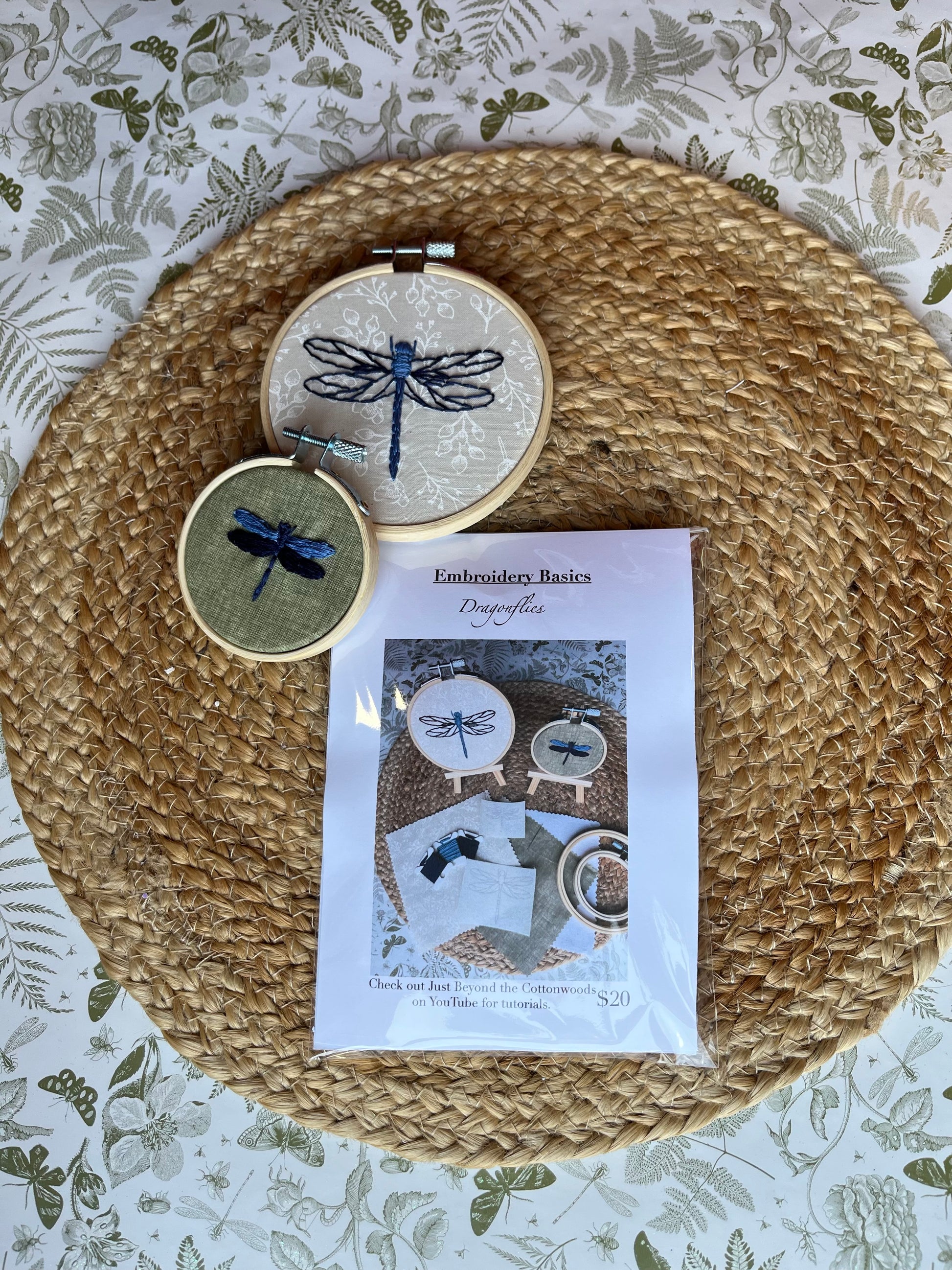 Embroidery hoops with dragonfly designs on a woven mat with a patterned background