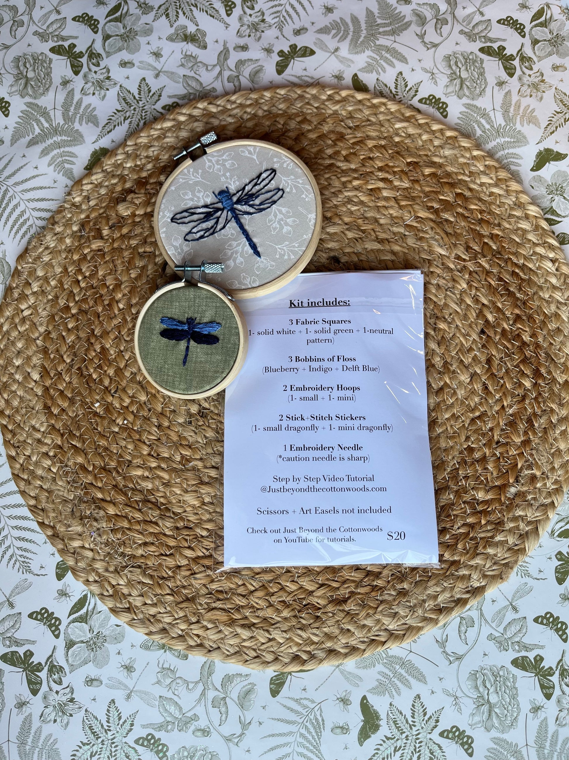Embroidery kit with dragonfly designs  with list of what is included in kit on a woven mat and patterned background