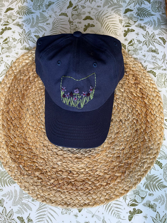 Navy blue cap with floral design on a woven mat with a floral patterned background