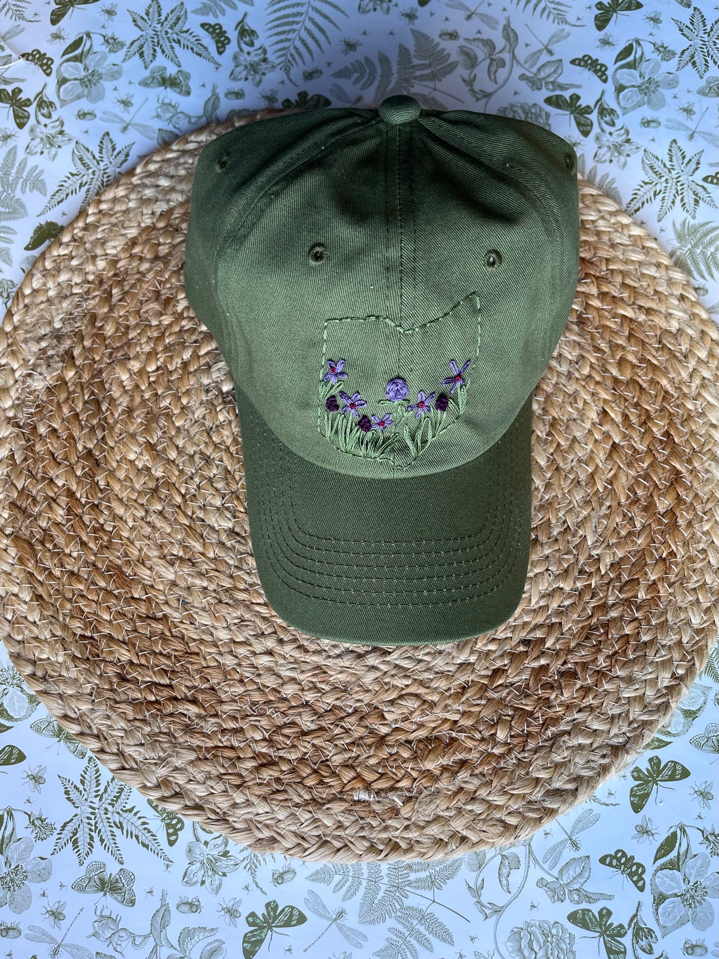Green cap with floral embroidery on a woven mat with a floral-patterned background