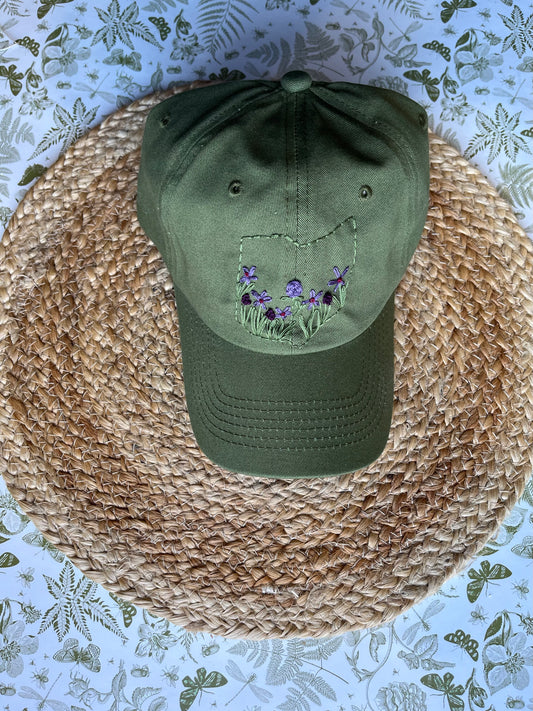 Green cap with floral embroidery on a woven mat with a floral-patterned background
