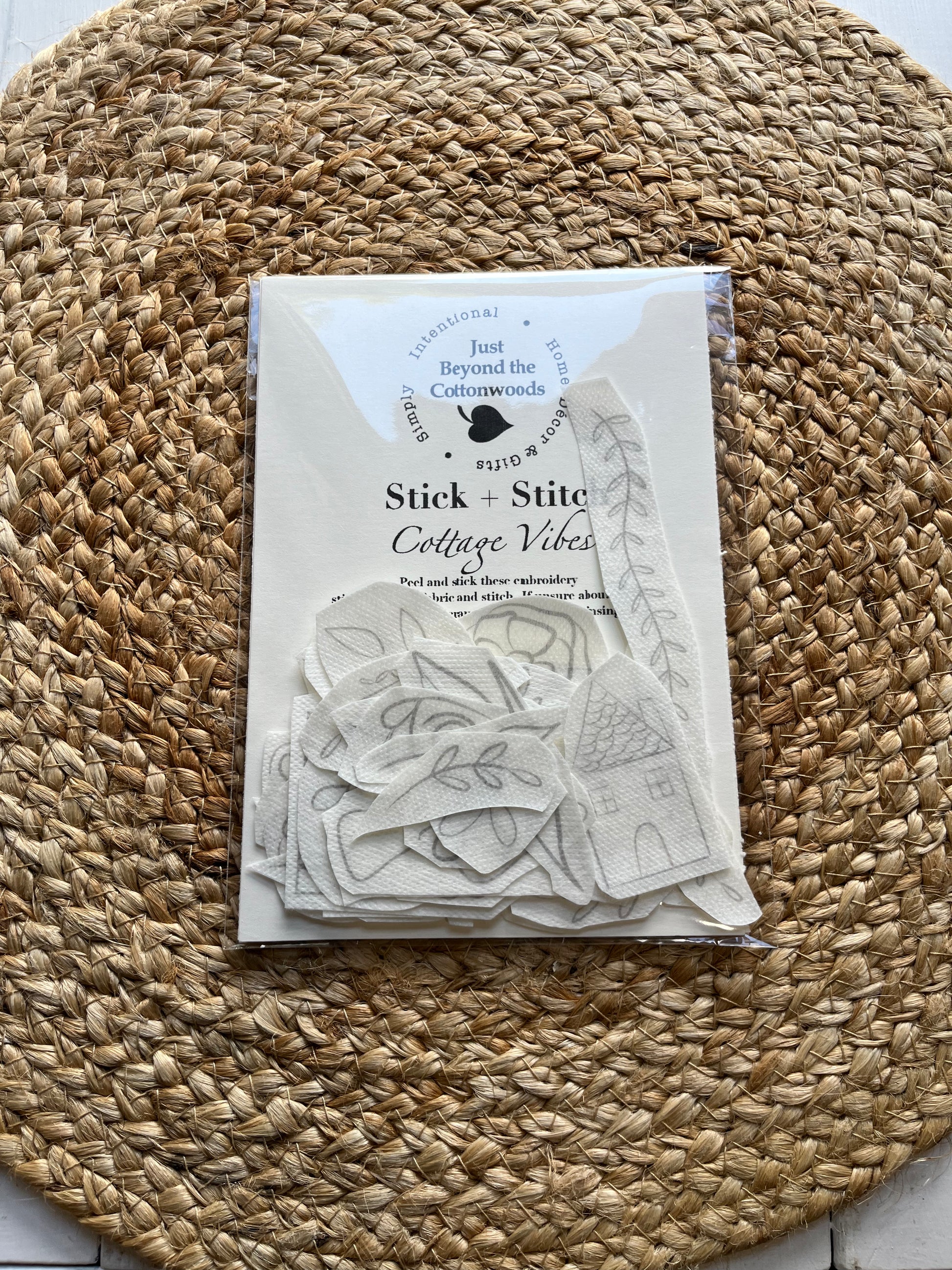 A set of hand-embroidery stickers with various floral and cottage vibes patterns, displayed on a woven mat, with a label in the foreground showing the product name and brand.