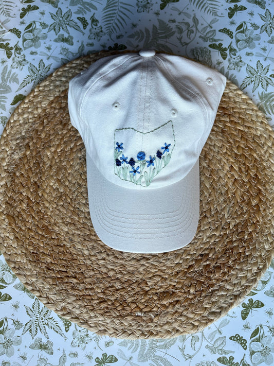 White stone cap with floral design on a straw hat against a floral-patterned background