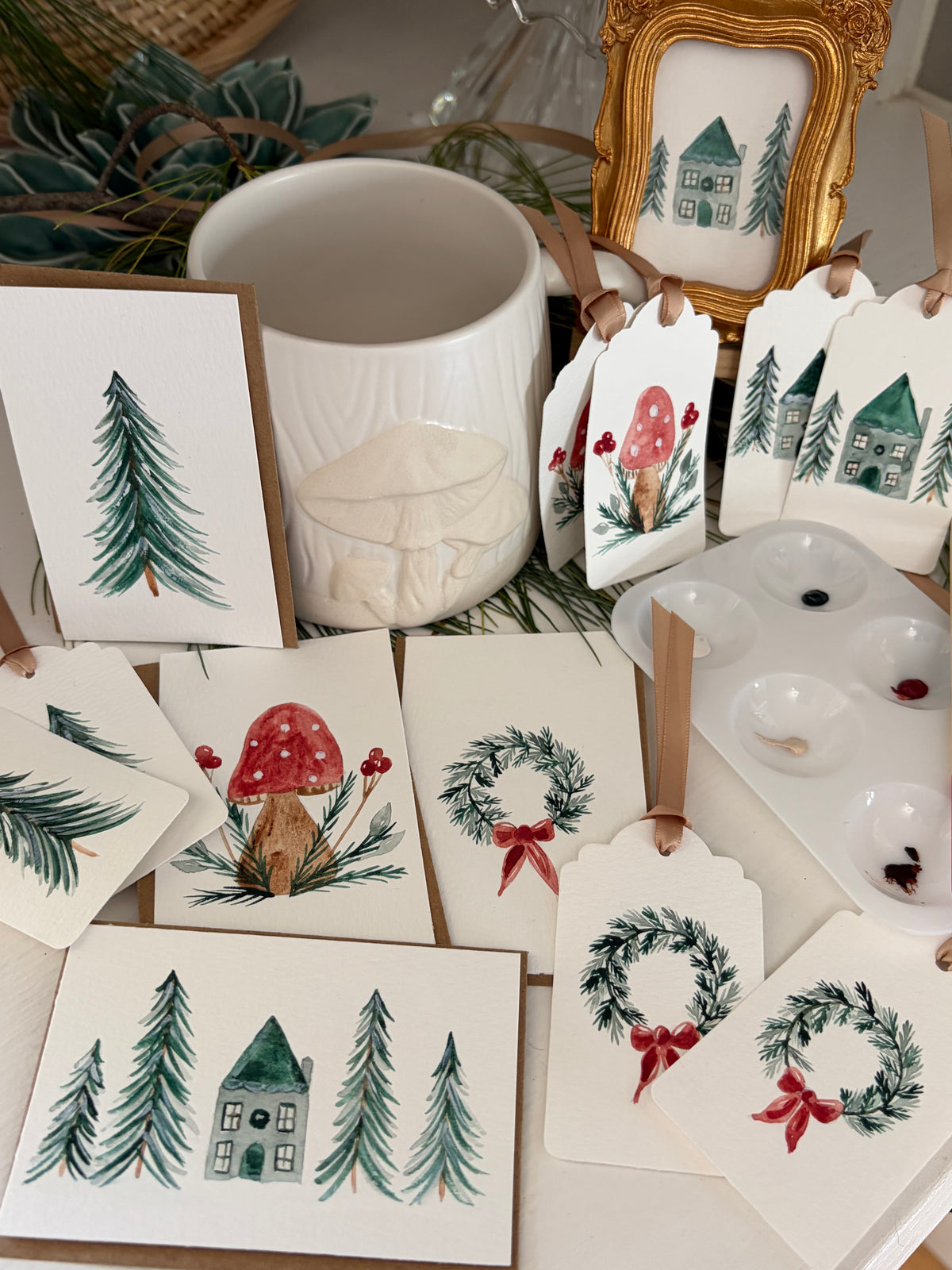 Hand Painted winter-themed greeting cards, gift tags, and a small framed print, with watercolor illustrations of pine trees, red-and-white mushrooms, and Christmas wreaths with red bows. 