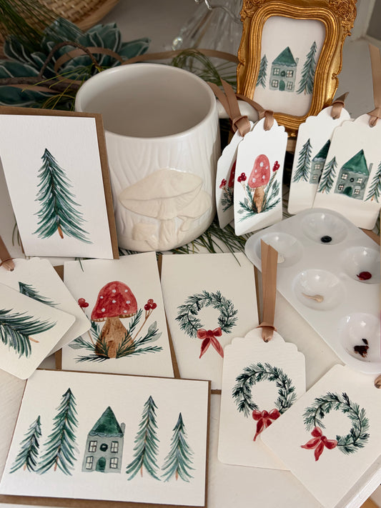 Hand Painted winter-themed greeting cards, gift tags, and a small framed print, with watercolor illustrations of pine trees, red-and-white mushrooms, and Christmas wreaths with red bows. 